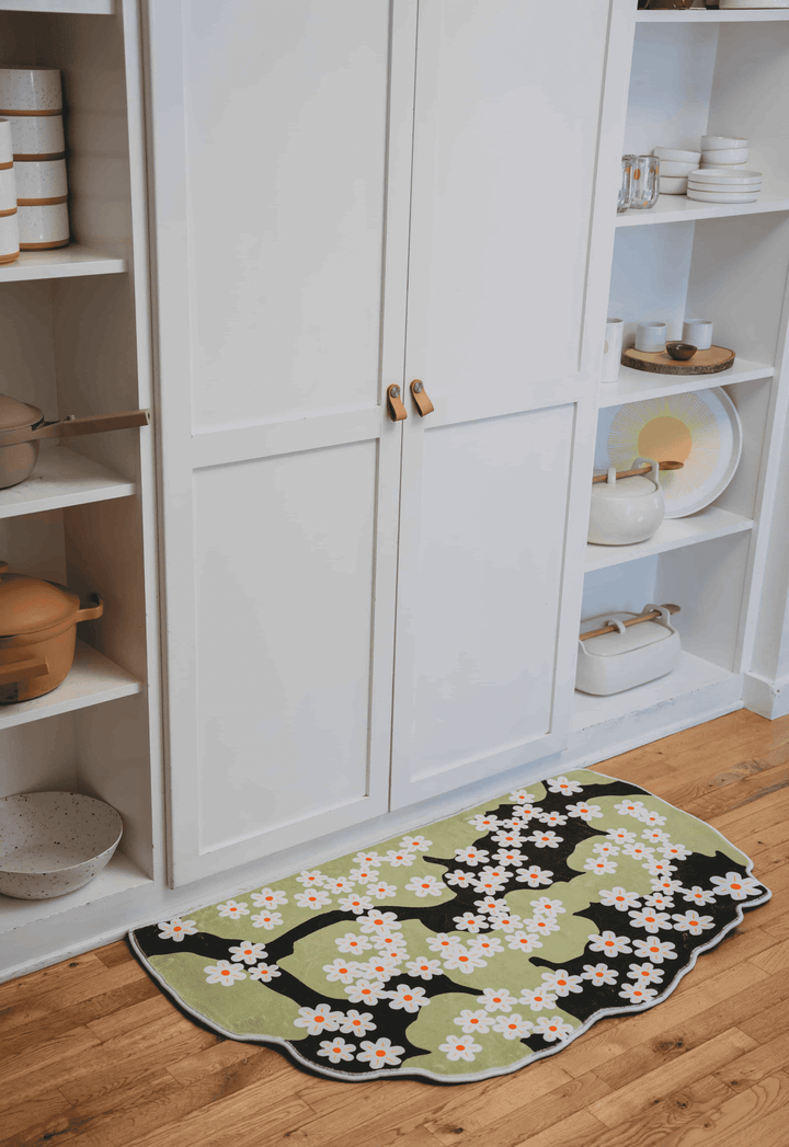 Daisy rug laid on wood floor in front of tall white cabinets, surrounded by open shelving with soft neutral tones.
