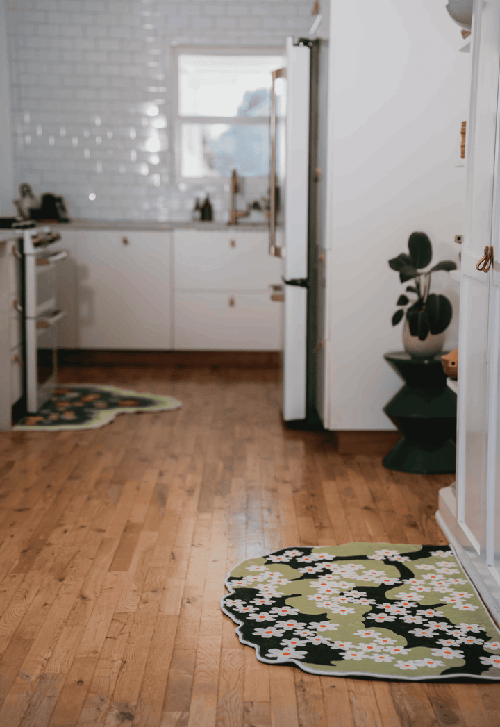 Two daisy rugs spread across wood floor in a long kitchen aisle, placed beside counters and cabinet edges.