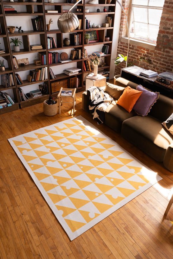 Yellow & pastel Triangle Dance Rug in a bright loft living room, paired with warm wood floors and a cozy book-filled wall