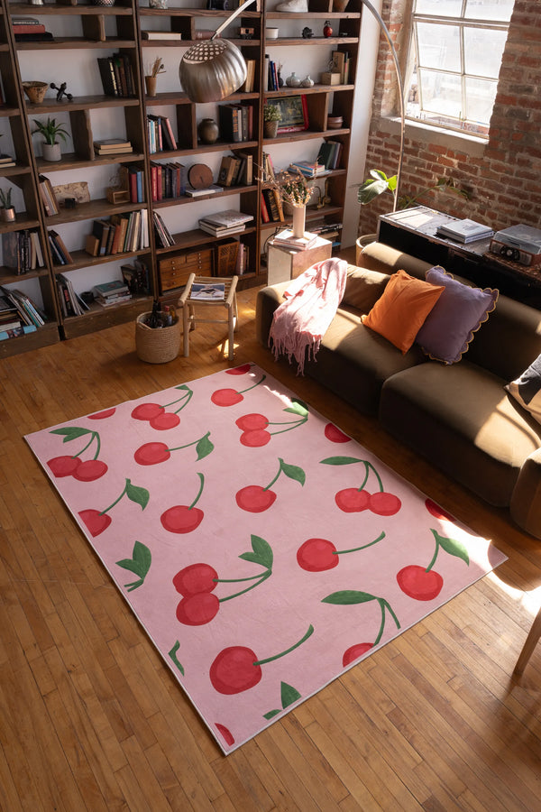 Cute pink rug with cherry pattern brightens a cozy living room with bookshelves, modern decor, and natural sunlight