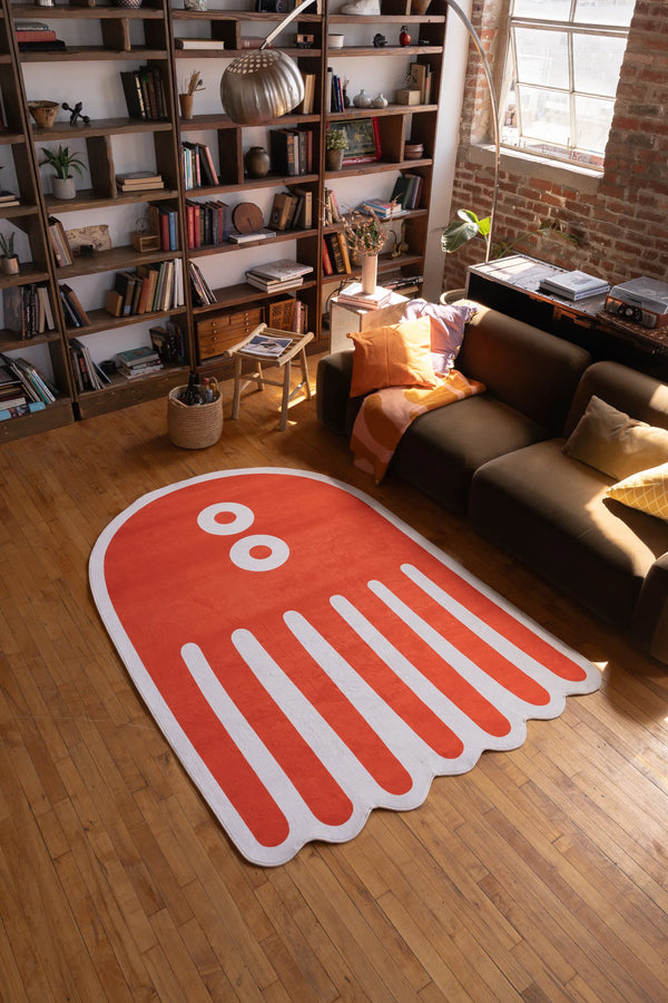 Large orange abstract octopus rug in 5x7 size on wooden floor in cozy living room with bookshelf and warm lighting