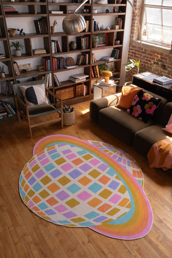 Colorful Disco Planet Rug by Darra Sargnt centered on wood floor, placed in front of a dark sofa with warm cushions and throw