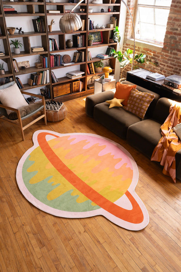 Melting Planet Colorful Rug by Darra Sargnt in a cozy living room with bookshelf, sofa, and wood floor.