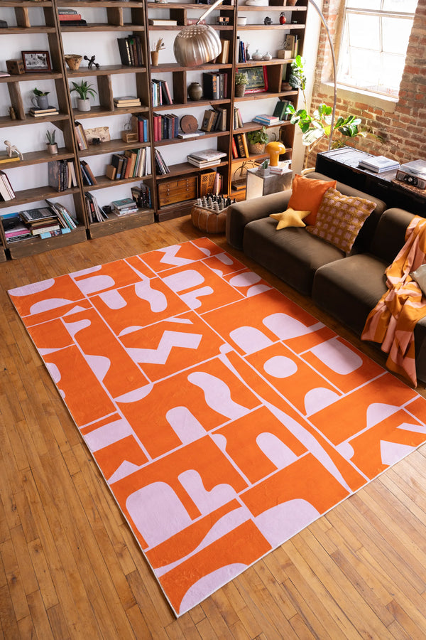 Orange Geometric Patchwork Rug by Becca Franks in a cozy room with shelves and sofa, modern abstract rug for living space decor