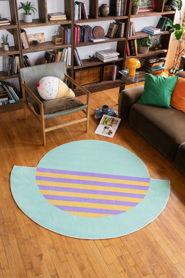 Modern area rug in mint green with yellow and purple stripes placed in a cozy reading corner with books and plants