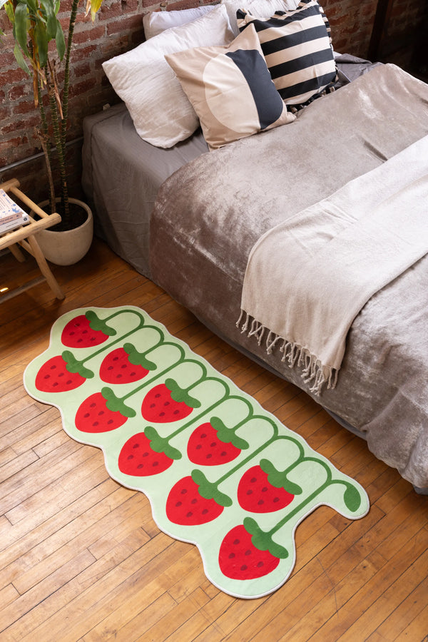 Red strawberry shaped bedroom rug on wooden floor next to neutral bed and modern nightstand – whimsical home decor