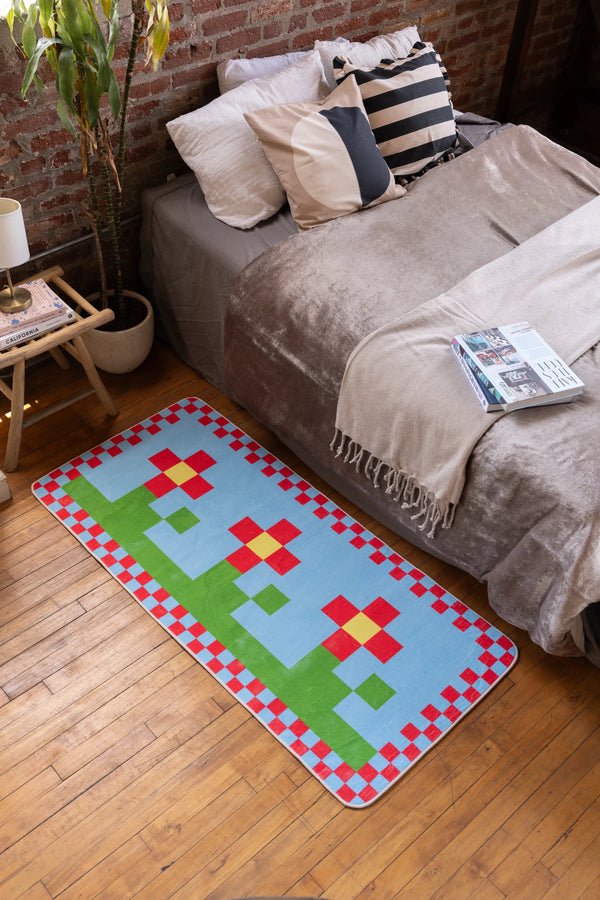 Bedside view of multicolor pixel flower rug with red, green, and yellow blocks on blue background