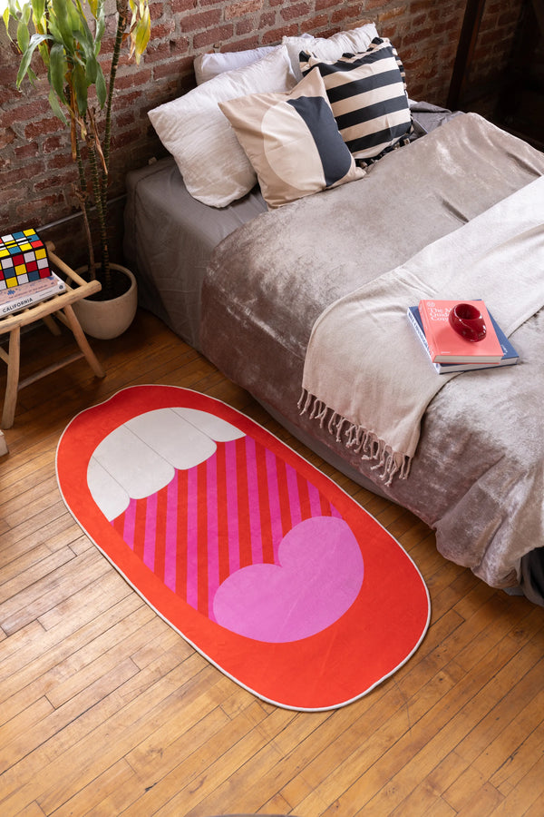 Red Mouth Pop Art Rug by Becca Franks beside bed in bold, cozy bedroom with wood floor