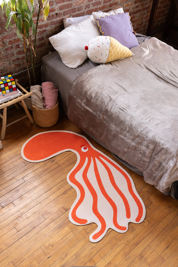 Orange Octopus Area Rug by Becca Franks beside bed in cozy brick-walled bedroom with plush bedding
