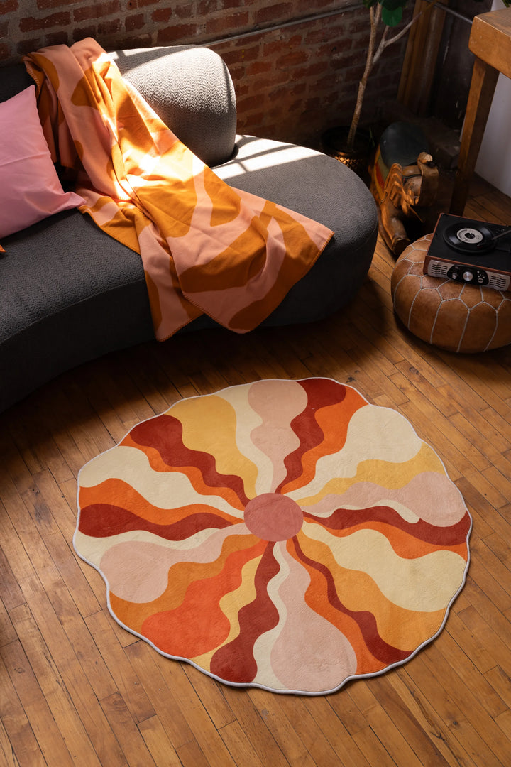 A scalloped orange rug with radiating waves on the wooden floor in front of a curved sofa.