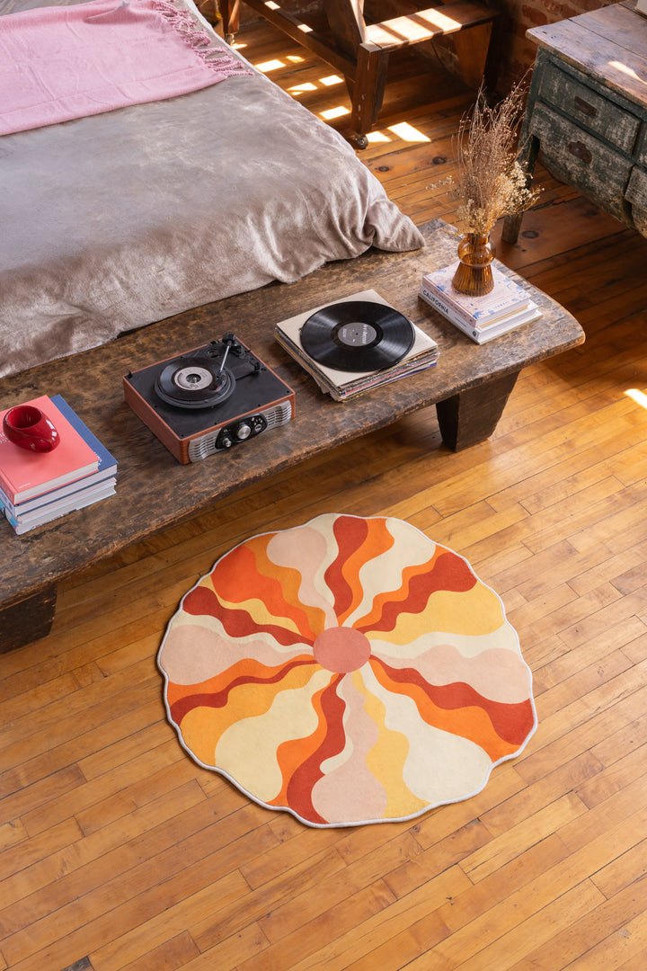 Round sundial orange rug placed beside a rustic wooden bed bench, adding a burst of warmth to the wooden floor.