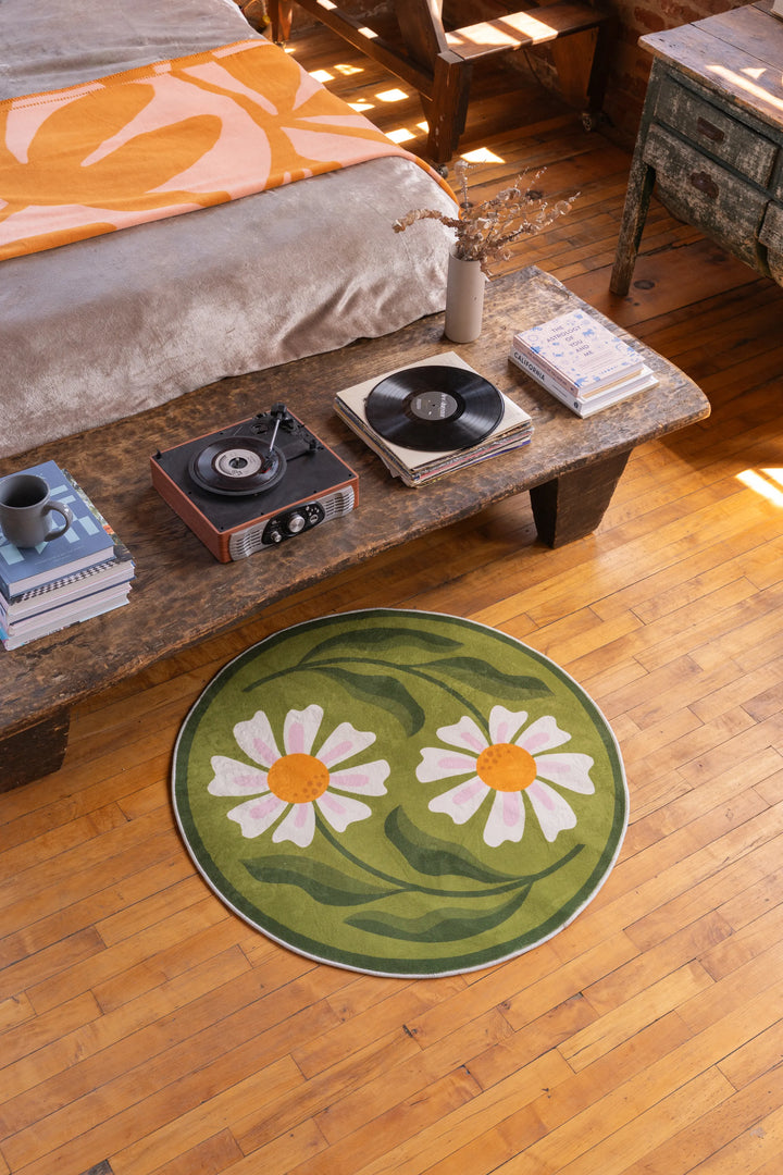 Green daisy rug adds a soft botanical charm to the bedroom with wooden floors and a rustic coffee table.
