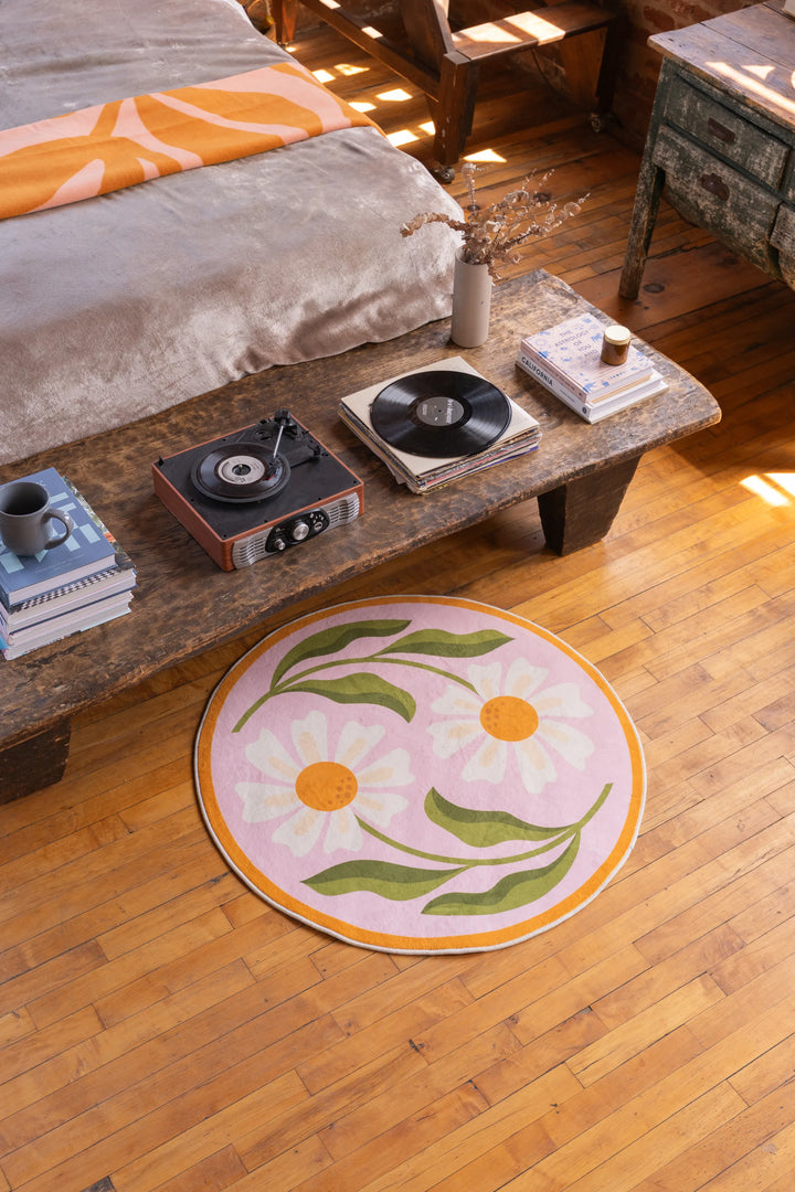 Dual Daisy Round Rug by Jessica Miller placed in front of a rustic wooden table and daybed on warm wood floor.