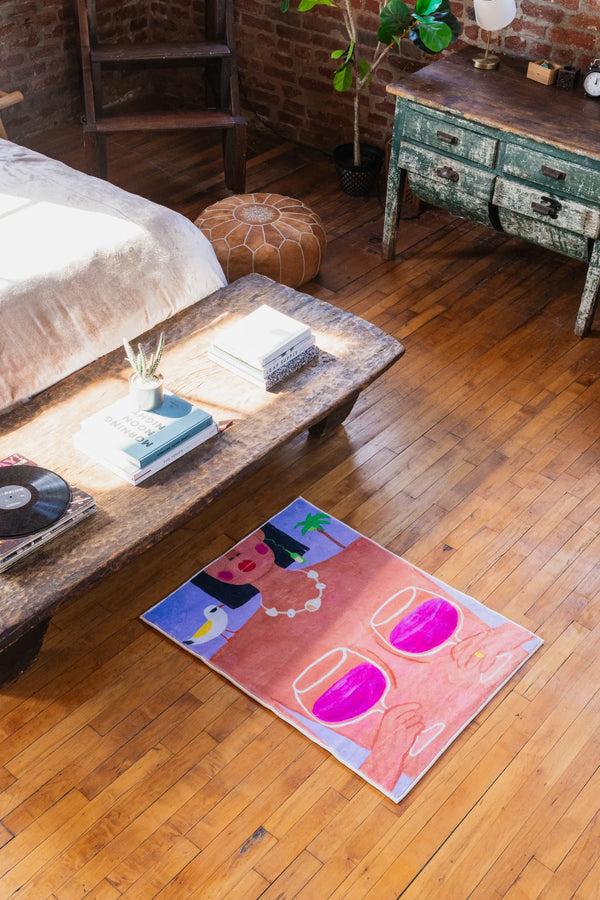 Small 2.2'X3' funky wine and woman rug tucked under rustic coffee table in bedroom, angled shot with sunlight on wooden floor.