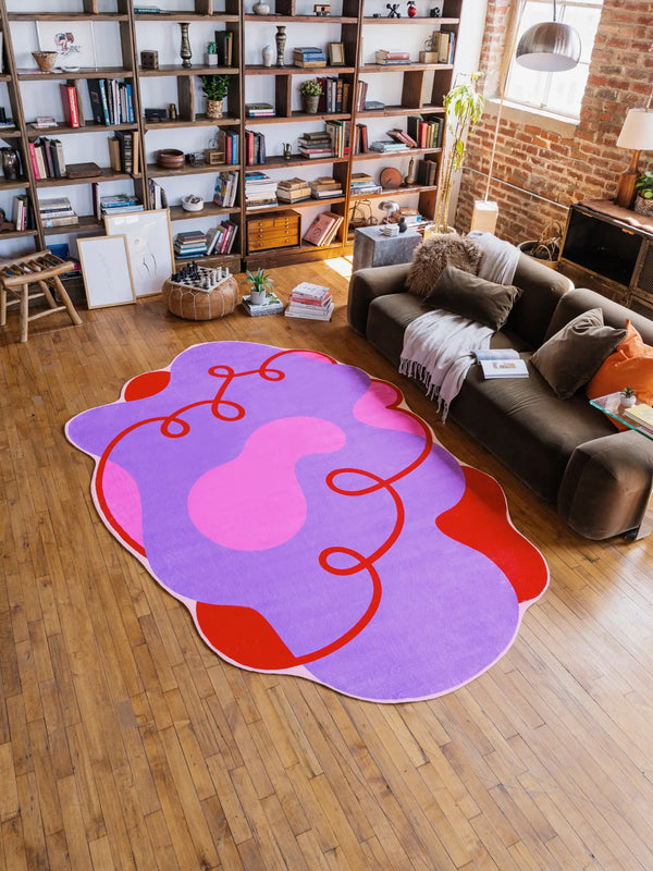 A purple irregular area rug with bold red swirls sits in the center of the living room, adding a vibrant pop of color against the brick wall backdrop.