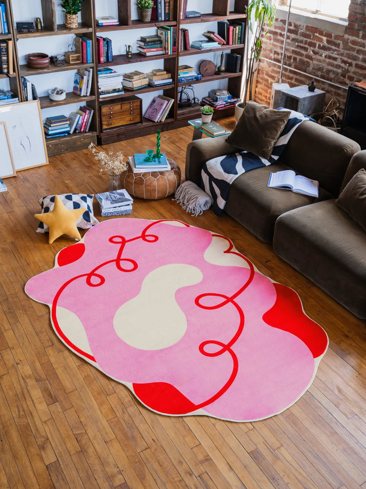 Large 5'X7' funky pink rug with curvy red accents, spreading across the wooden floor to anchor a colorful living room.