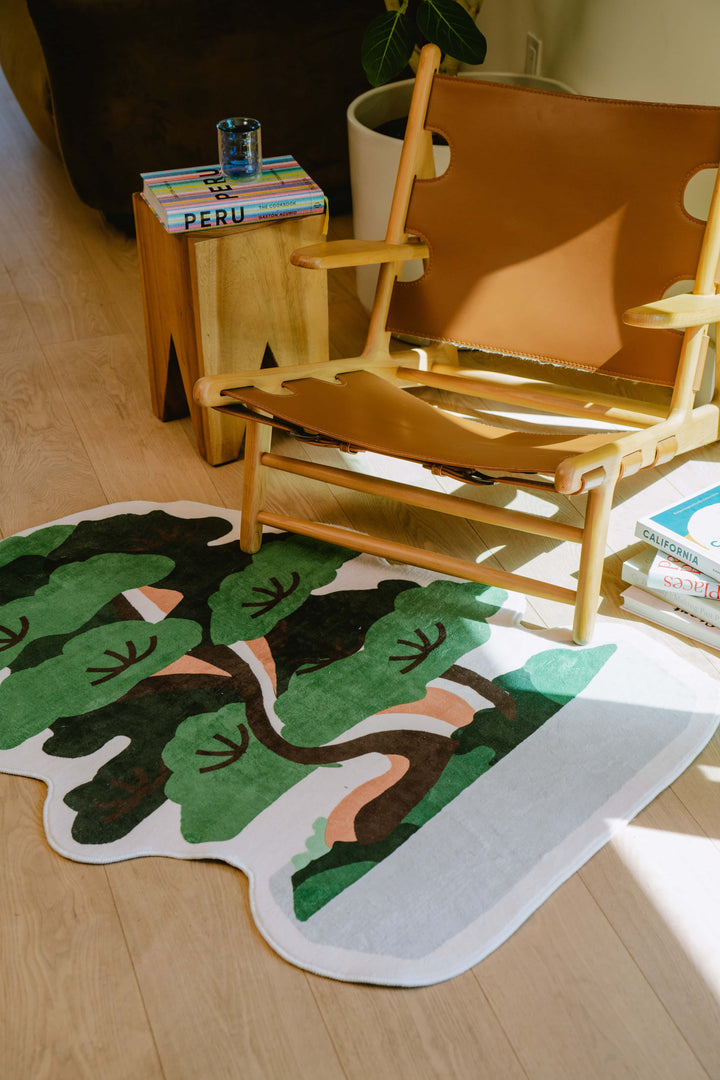 Close-up of the potted tree runner rug under a tan leather armchair with books and a side table.