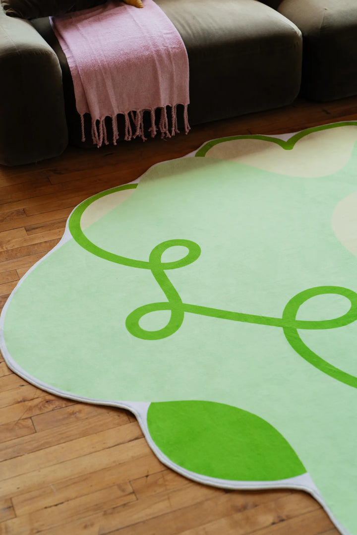 Light green funky rug with dark green swirls, partially shown near a sofa draped with pink throw, highlighting modern playful design.