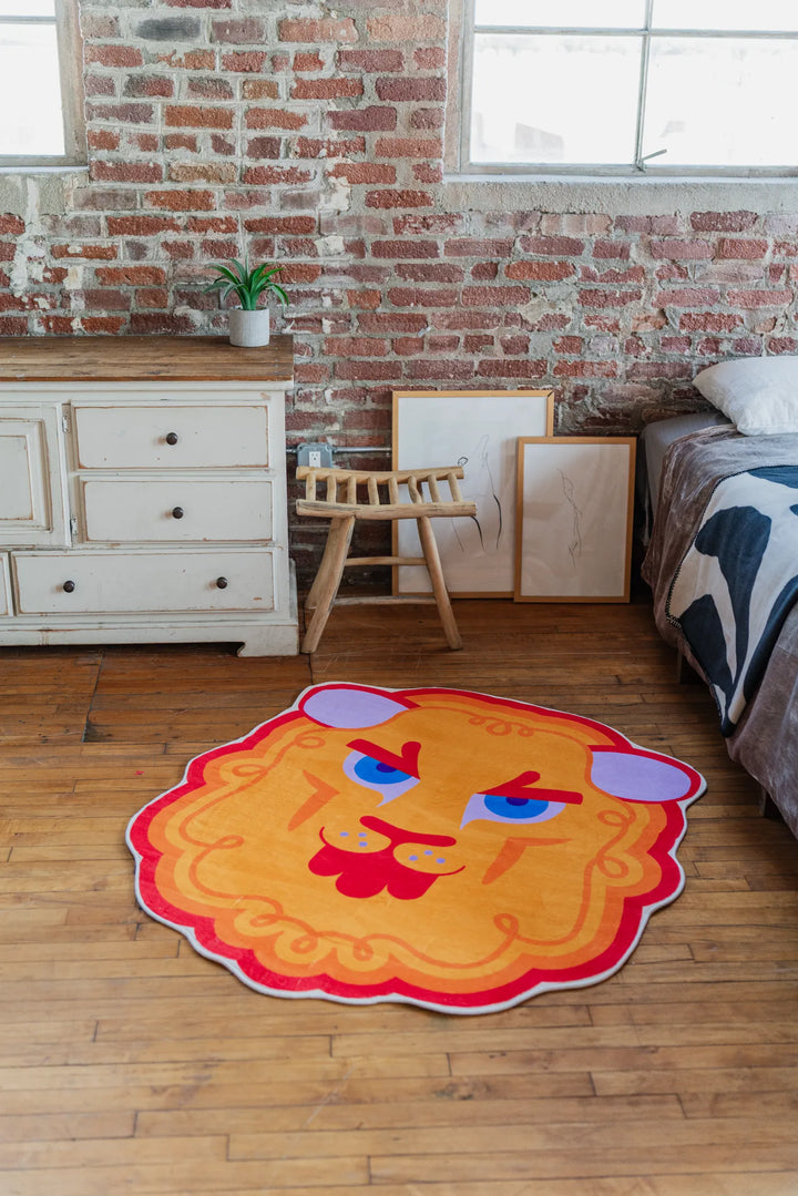 Cartoon lion head shaped rug by Shayla Goethe placed on wood floor near a rustic dresser and exposed brick wall.