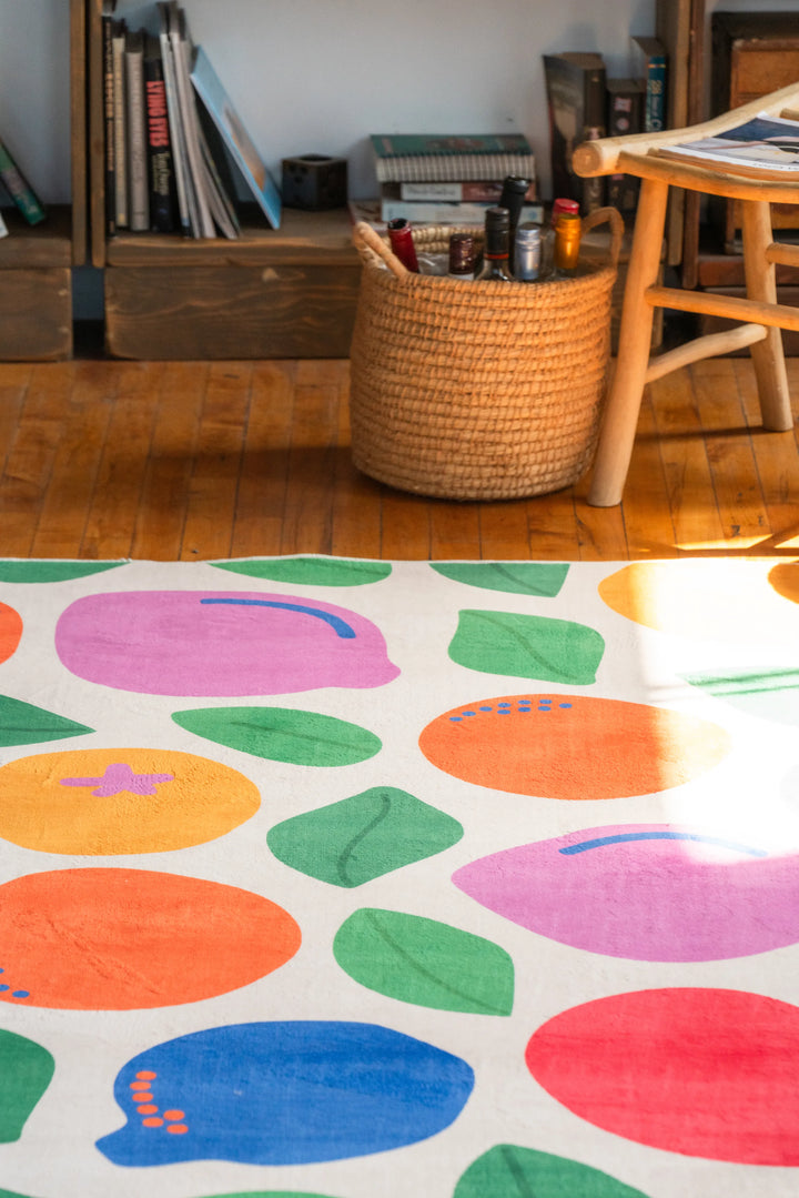 Colorful pastel rug with fruit motifs placed neatly on wood floor beneath filtered sunlight
