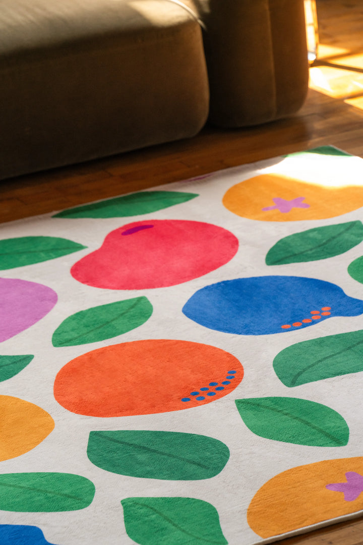 Pastel Fruit Party Rug by Becca Franks placed in front of a dark sofa on wood floor with natural light