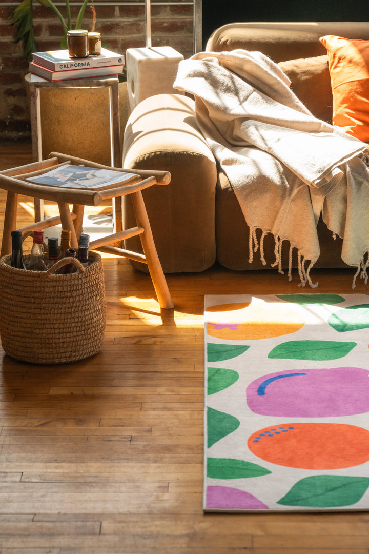 Pastel fruit party rug beside a sofa, partially lit by sun, with vibrant prints standing out on the wood floor