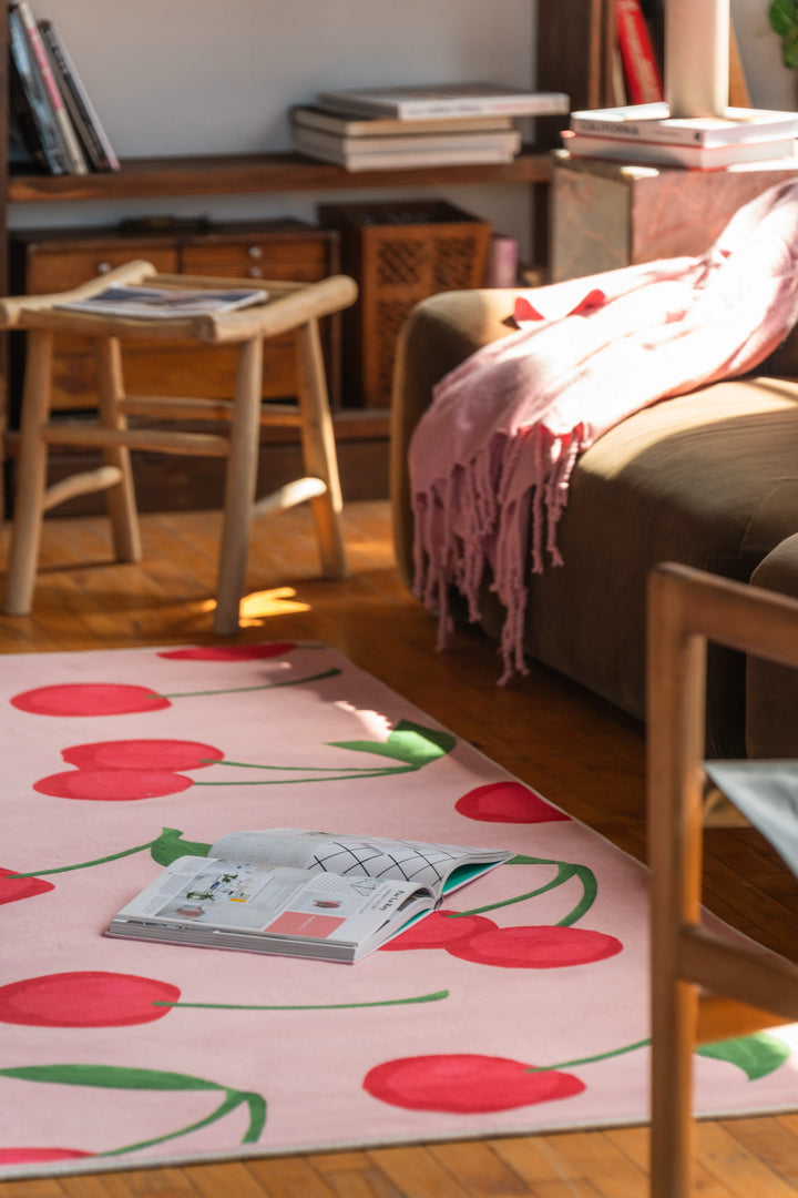 Detail of a cute cherry rug on wooden floor with magazine and soft brown sofa, adding charm to a sunlit living space