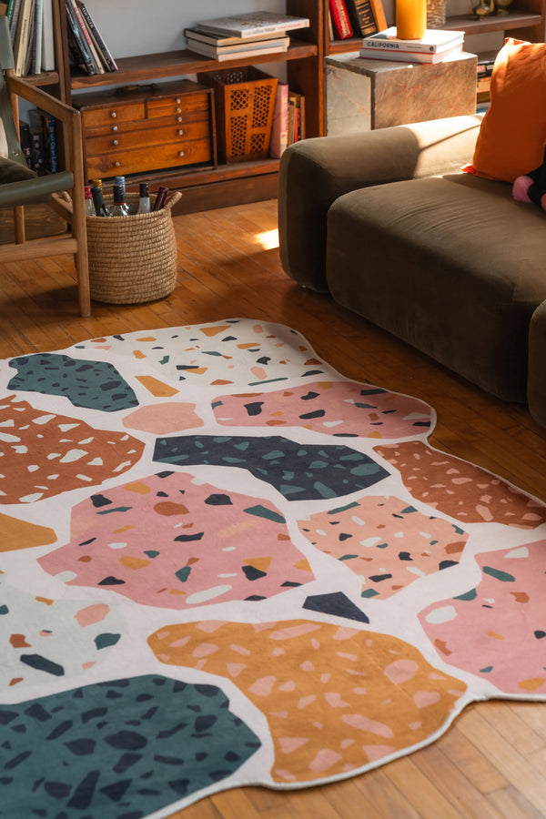 Close-up of colorful mosaic rug beside a brown couch, featuring soft texture and abstract patch shapes in warm tones