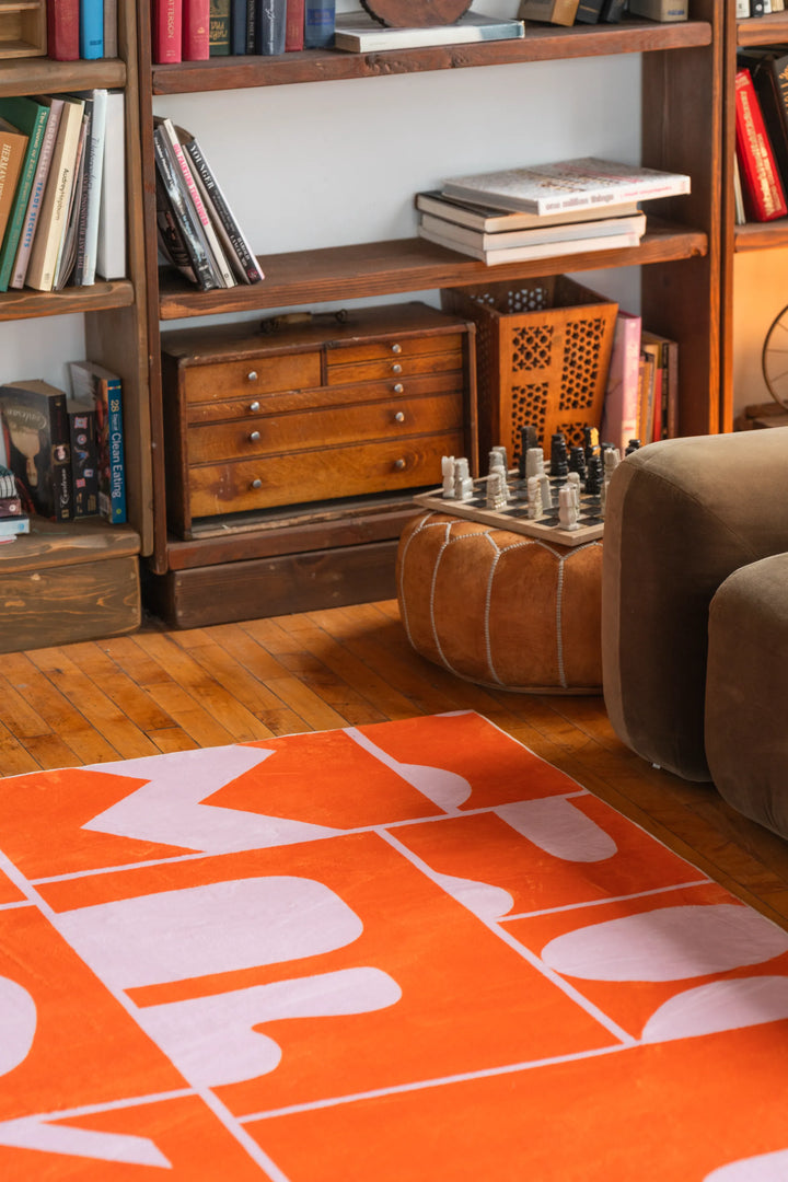 Orange Geometric Patchwork Rug partially styled near a brown armchair and wood bookshelf, modern rug with abstract pattern