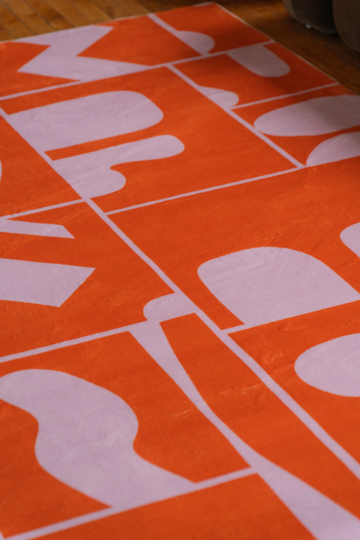 Close-up view of the Orange Geometric Patchwork Rug by Becca Franks, showcasing its playful pattern on warm-toned wood flooring