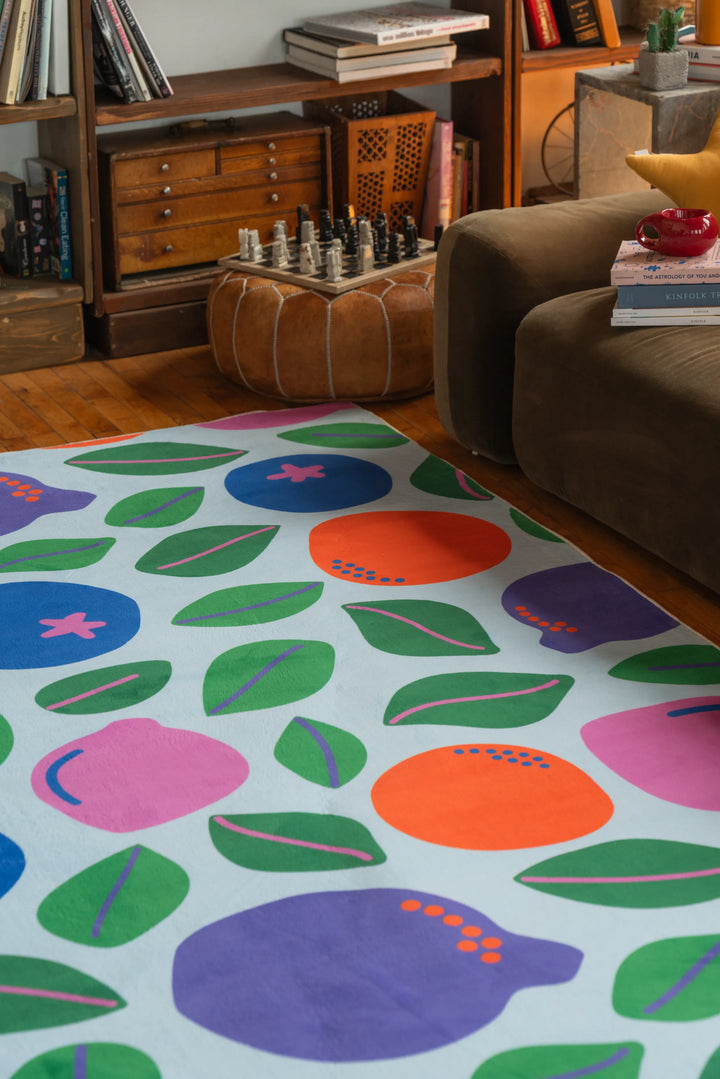Funky rug in vivid fruit shapes placed next to a brown sofa and wood drawers, adding pop to the corner