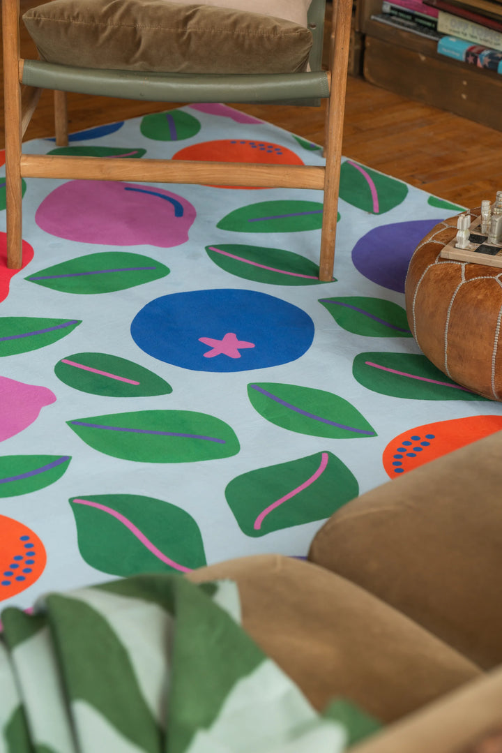 A playful rug with colorful fruit shapes extends beneath armchairs and pouf on wood floor