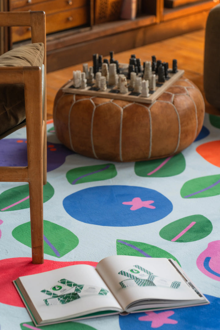 Funky rug with fruit motifs tucked between chairs and soft seating in a warm, book-lined nook