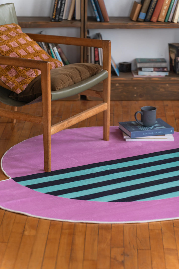 Close-up of a pink designer rug with teal and black stripes under a wooden armchair in a warm-toned living room