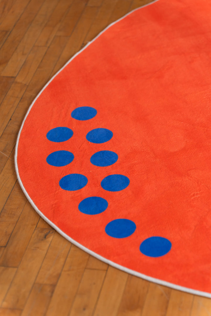 Close-up of blue dot pattern on edge of round orange minimalist rug lying on hardwood floor