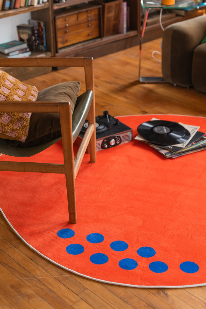 Close-up of Orange Minimalist Rug by Becca Franks with blue dots, vinyl records and chair legs in frame