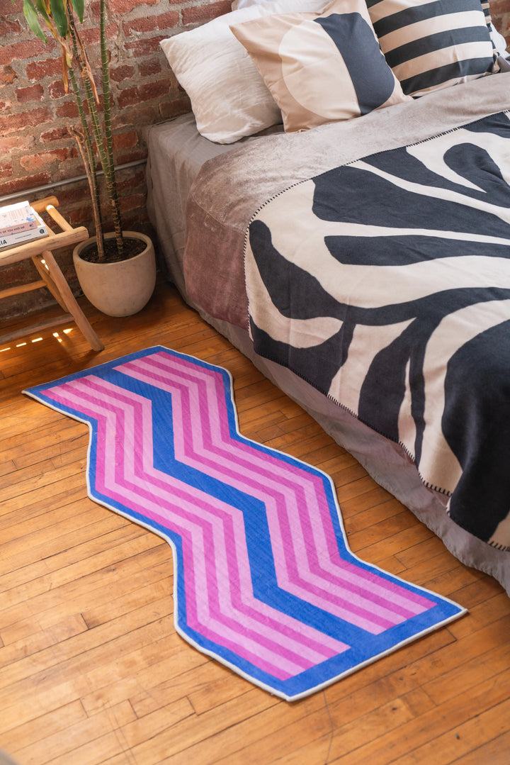 Colorful zigzag bedroom rug in pink and blue tones next to bed with zebra print sheet