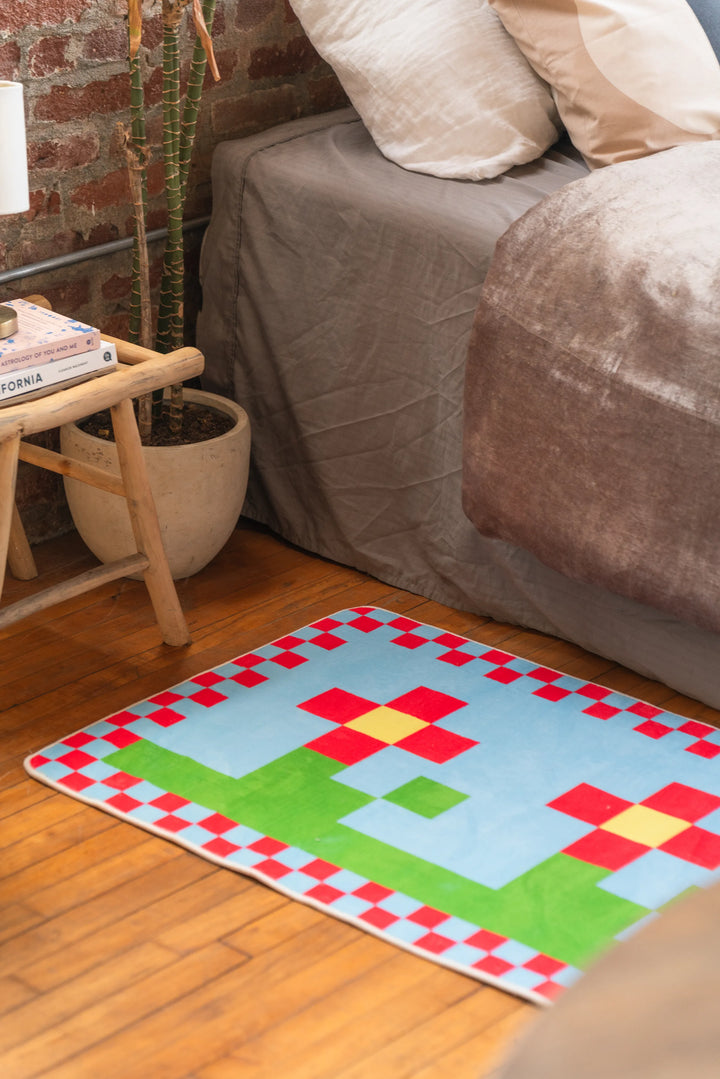 Close-up of multicolor pixel flower rug next to nightstand and plant