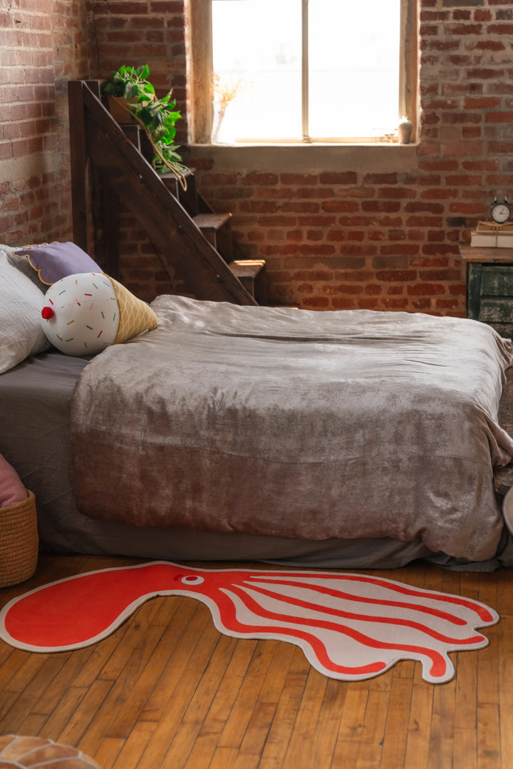 Playful orange octopus-shaped area rug on wood floor next to bed in sunlit bedroom
