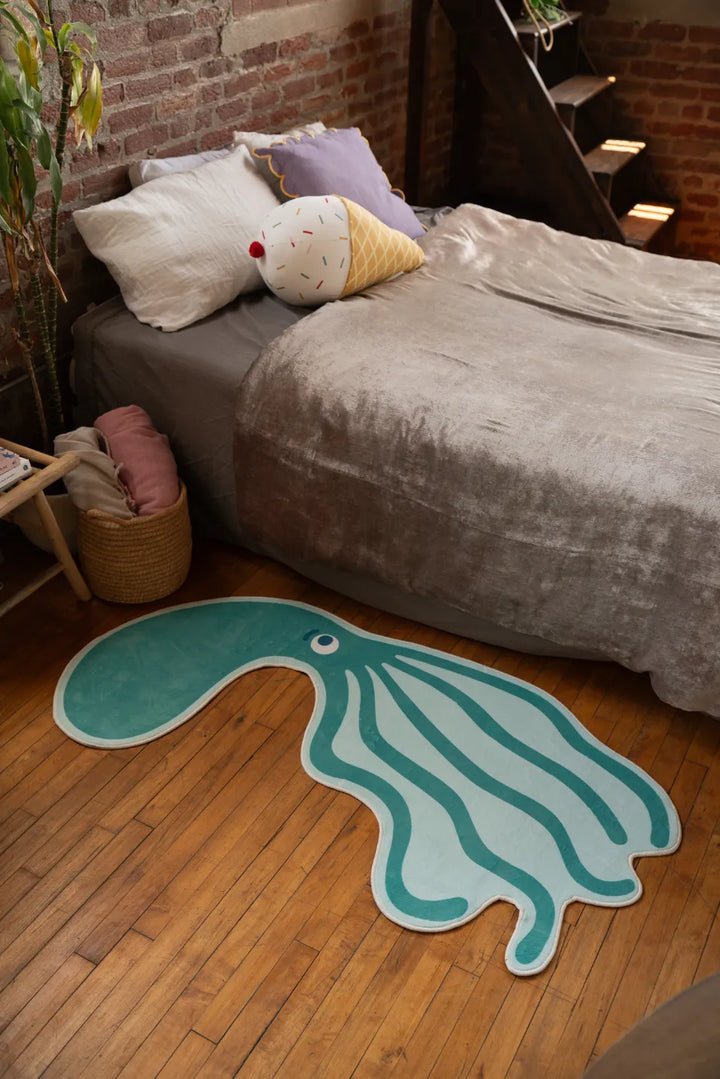 Green Octopus Area Rug by Becca Franks beside bed in cozy bedroom with warm wood floors