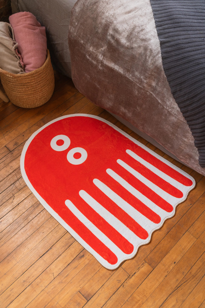 Playful orange rug with eye design sits on wood floor next to a beige bed and a basket filled with pink bedding