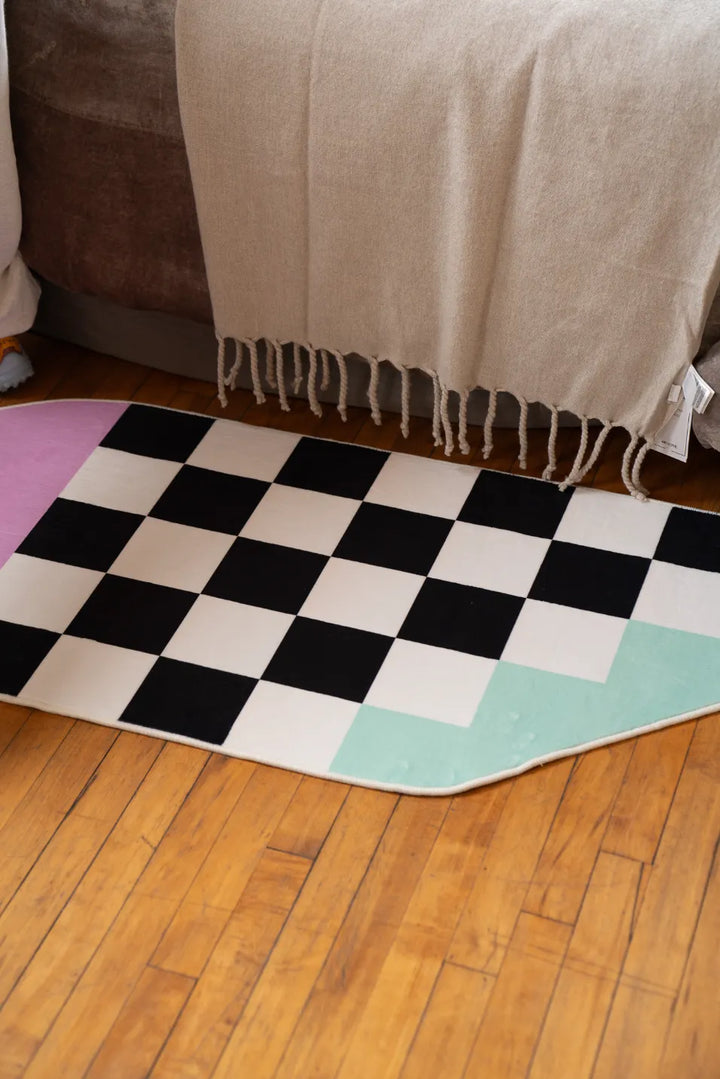 Pink and Blue Asymmetrical Checker Rug laid neatly along one side of the bed, catching window light on wood floor