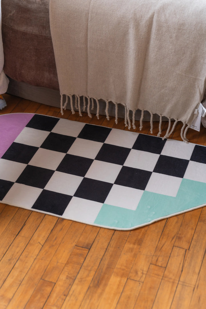 Funky checker rug aligned closely along bedside on wood floor, creating a clean edge transition