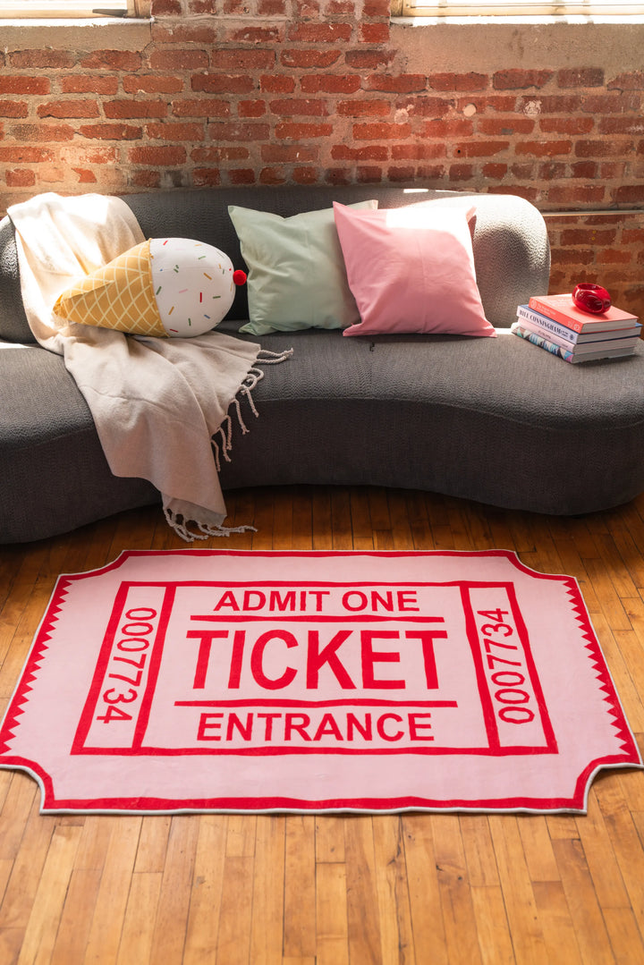 Graphic red ticket-shaped living room rug placed in front of curved sofa under sunlit window