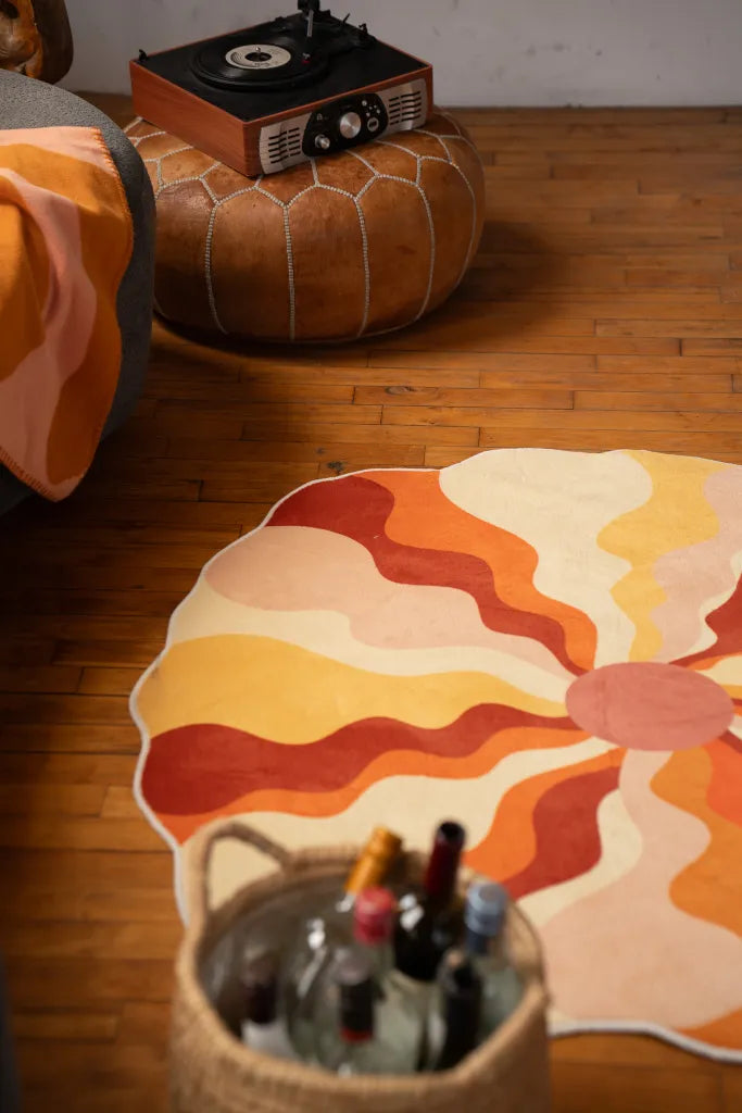 Close-up of a wavy orange rug next to a basket of bottles and a leather ottoman with a record player.