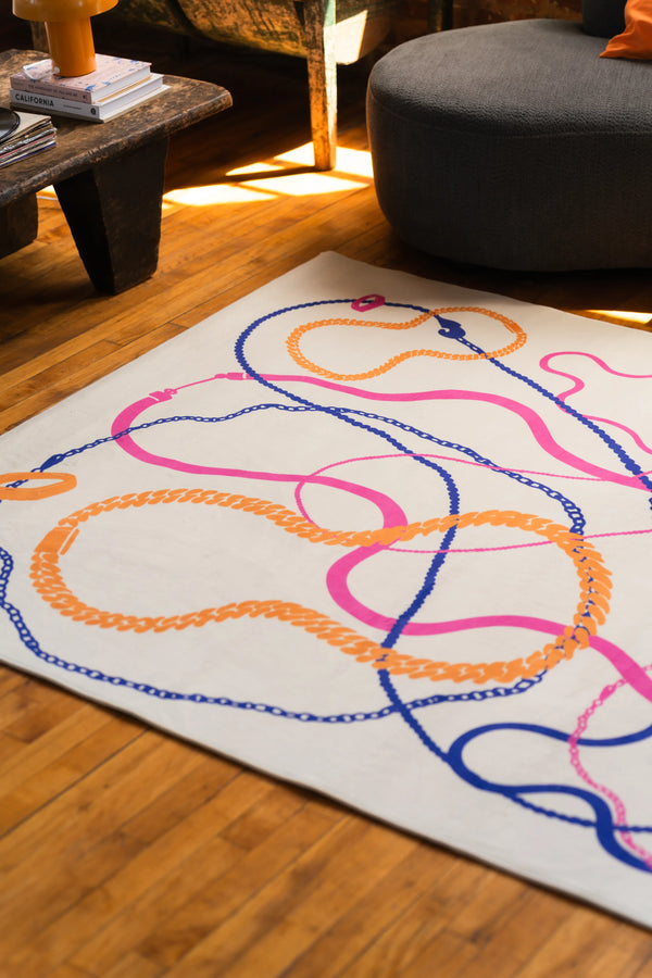 Cream rug with colorful winding lines in orange, pink, and navy placed in a sunlit corner of a cozy living room
